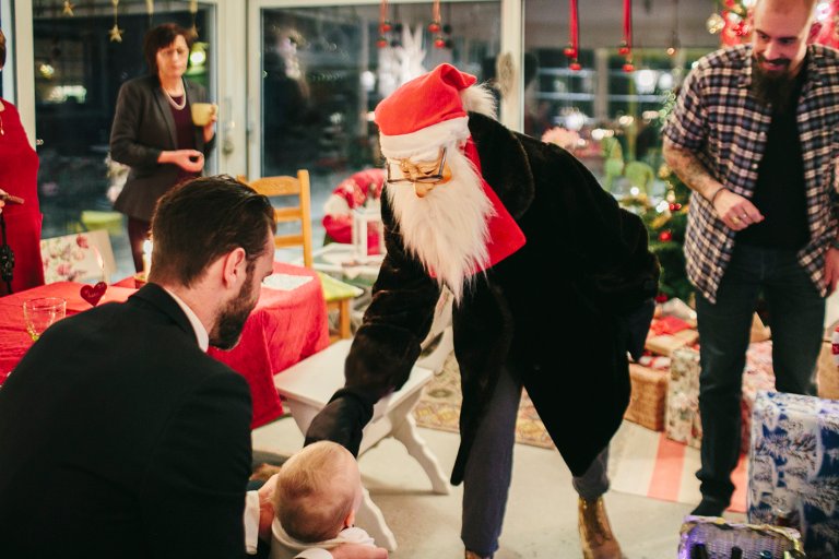 Bilde av julenisse som deler ut gaver i et vanlig hjem. 