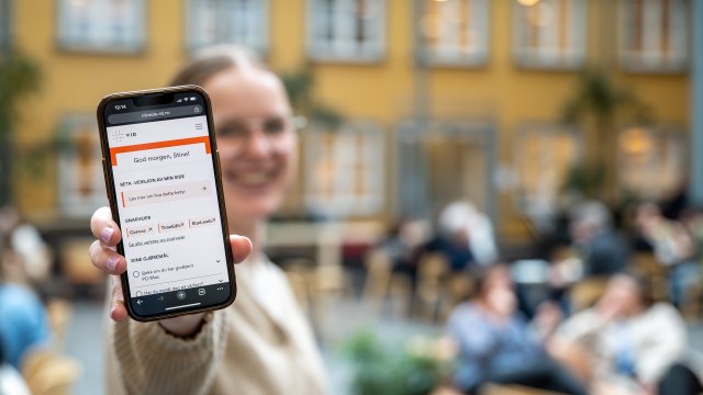 Person i bakgrunn som viser fram Min side plattformen på sin mobil