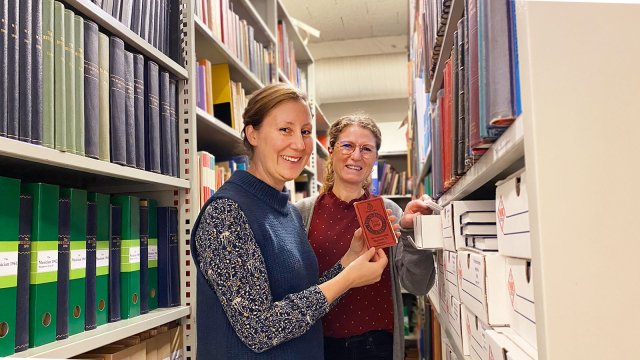 To damer tar ut en liten bok fra arkivhyller