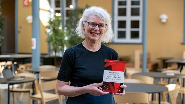 Inger Marie Lid står og holder boken i hendene inne i atriet ved VID Oslo.