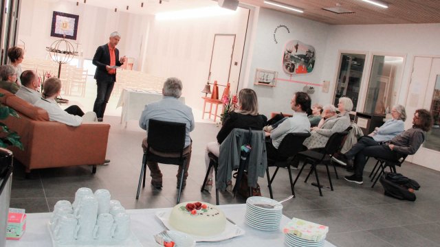 Mann som står og snakker foran en forsamling inne i et kapell.