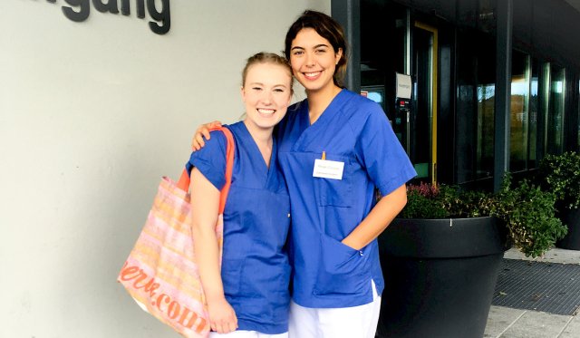 To smilende studenter i sykepleieuniform poserer