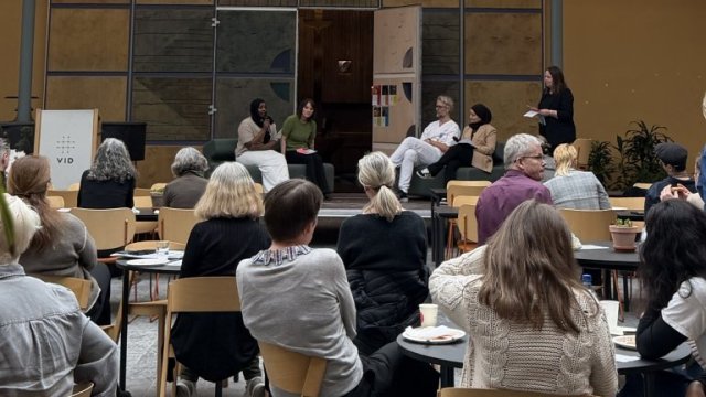 Publikum sitter og ser mot scene med paneldeltakere