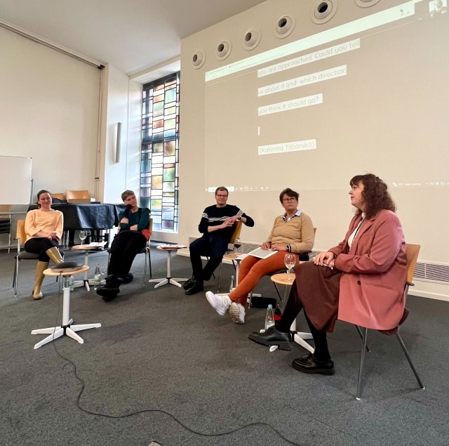 Fem personer sitter oppe på scenen i et panel