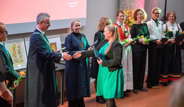 Rektor og prorektor deler ut diplom til doktorand. De andre doktorandene står på rekke og ser på.