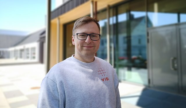Portrett av Roman Reindal som står utenfor inngang av VIDs bygg i Stavanger