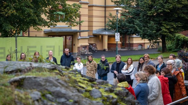 En gruppe mennesker står ute i en sirkel foran et gult bygg