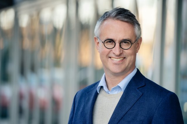 Portrettbilde av mann i blå blazer og skjorte med briller. Rektor Bård Mæland