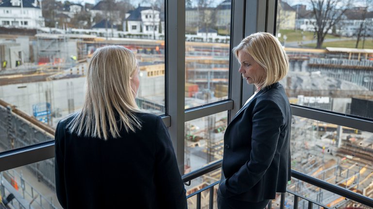 Gunhild Odden og Sigrun Aasland står foran vinduer og ser utover byggegropen
