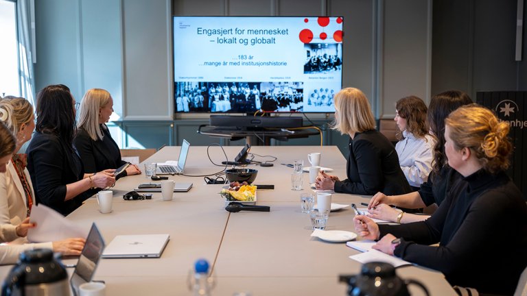 møterom der alle ser på powerpoint der det står "engasjert for mennesket -  lokalt og globalt"