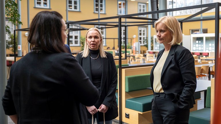 bilde av de tre som står og snakker i atriet.