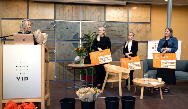 Alle fire står på rekke på scena. De tre masterstudentene holder hver sin store sjekk på 10.000
