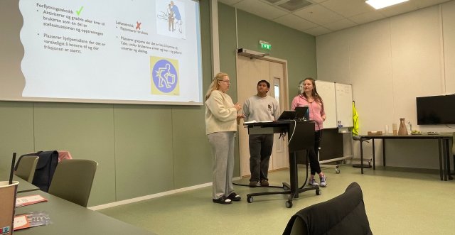 Tre studenter står å holder et foredrag med powerpoint