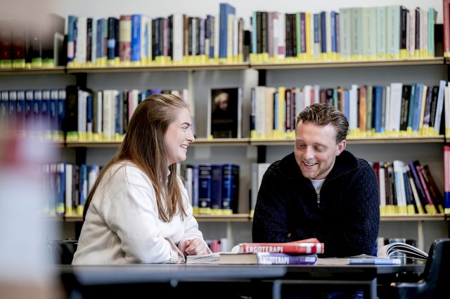 To studenter sitter på et bibliotek og smiler