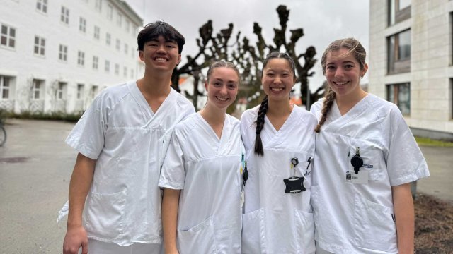 Bilde av fire sykepleie-studenter i hvite uniformer foran et sykehus