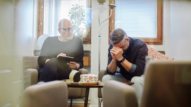 mann på sosialkontoret sitter med hodet i hendene sammen med terapeut