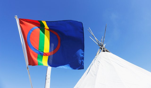 Samisk flagg som vaier i vinden foran en lavvo