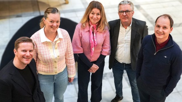 Portrett av de fem stående på rekke innendørs. 