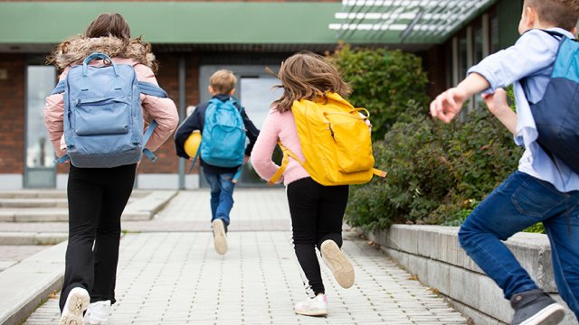 barn med skolesekk løper mot inngangen på skole