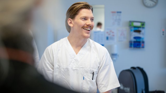mannlig sykepleierstudent i uniform. smiler og ser til siden.
