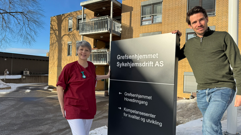 Portrett av Aina og Emilian stående på hver sin side av skiltet til Grefsenhjemmet.