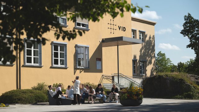 bilde av campus Oslo tatt utenfra. Studenter sitter utenfor hovedinngangen.