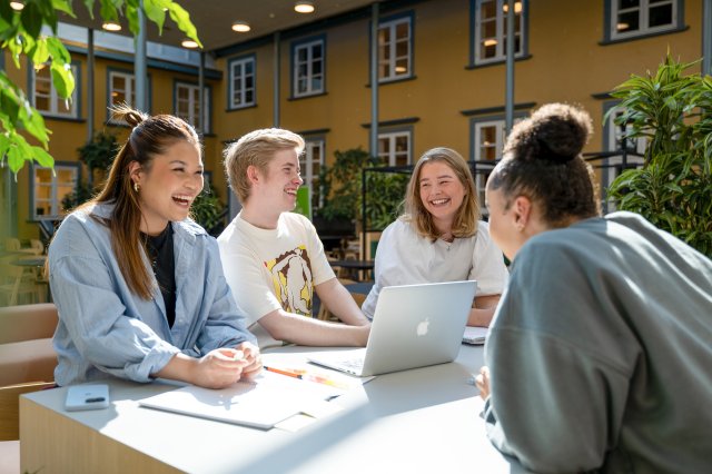 Studenter sitter i solfylt atrie og snakker sammen