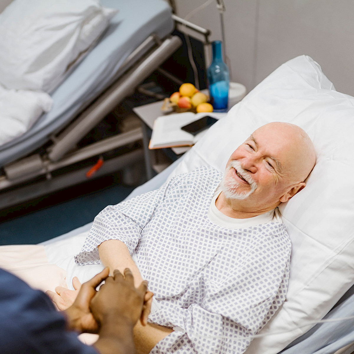 En pasient ligger i sykesengen og ser smilende opp på sykepleieren