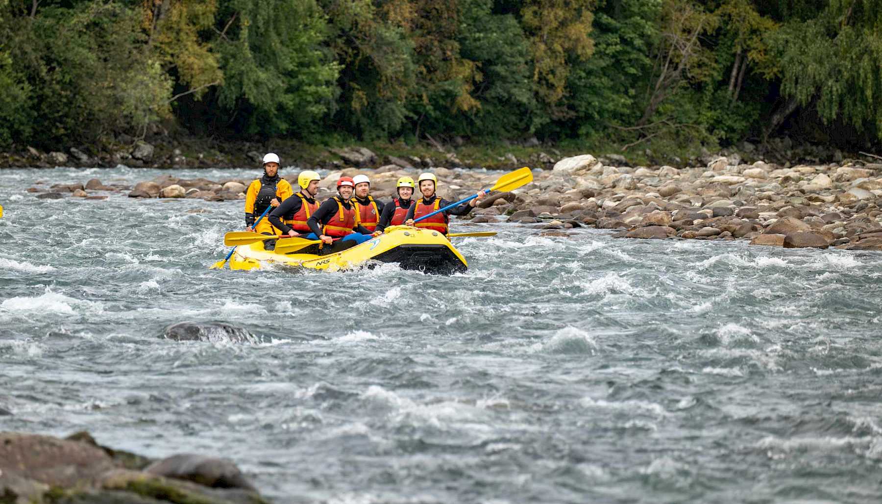 En gul raftingbåt med mange passasjerer rafter nedover en brusete elv