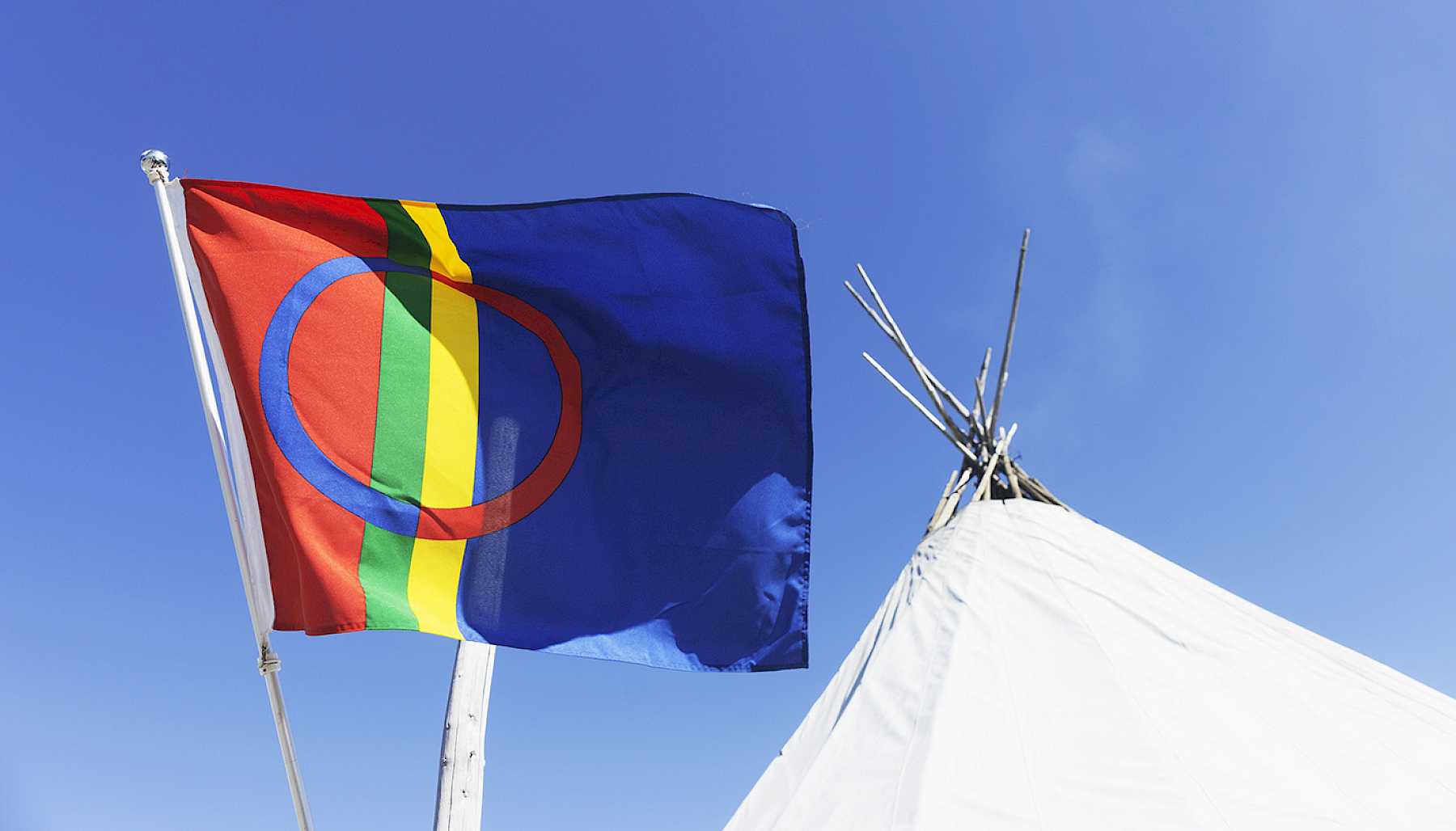 Samisk flagg som vaier i vinden foran en lavvo