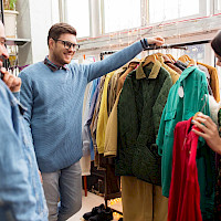 A man showing another man and a woman a green jacket at a clothing store