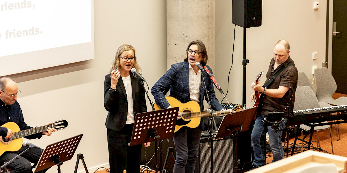 Bilde av musikere på scenen i Klara Lunde forelesningssal ved VID Bergen. To menn på gitar, en mann på bass og en dame som synger.