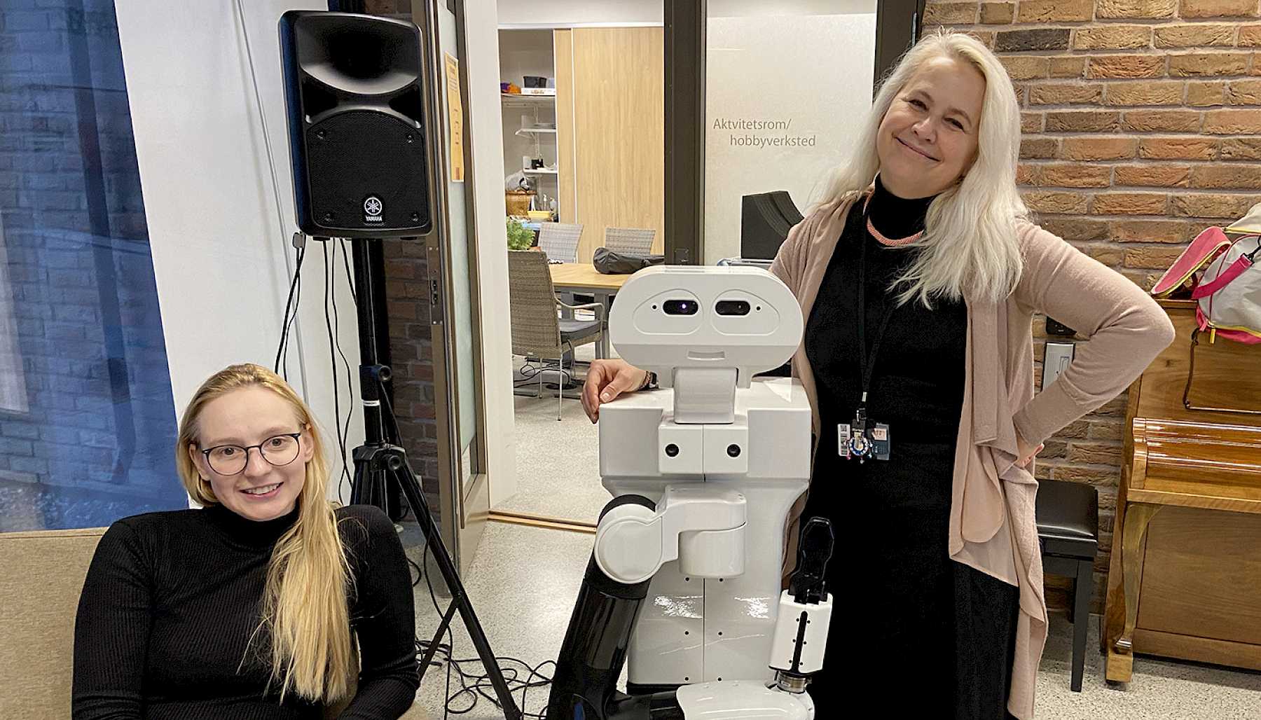 The two persons stand with a robot between them