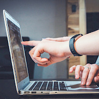 Nærbilde av en laptop med en hånd som peker på skjermen