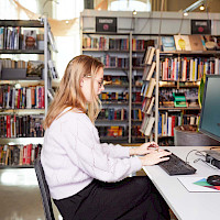 En kvinne sitter på en stasjonær pc på biblioteket