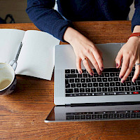 Et bord med en laptop, en notatbok og en tom kaffekopp