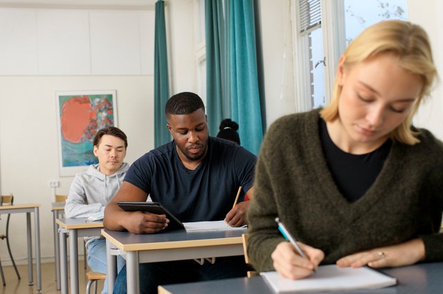 Tre studenter sitter i et klasserom og noterer
