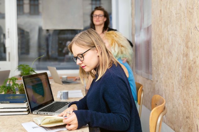 Ung dame med briller blar i en notatblokk og ser på en laptop mens huns studerer etisk refleksjon og veiledning.