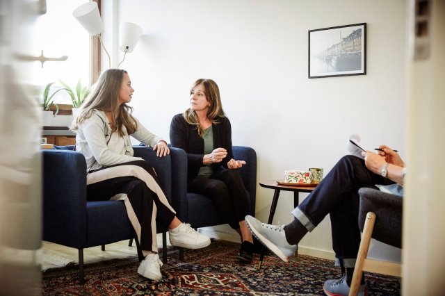 To damer sitter i en sofa og prater. Ved siden av sitter et annet menneske og noterer.