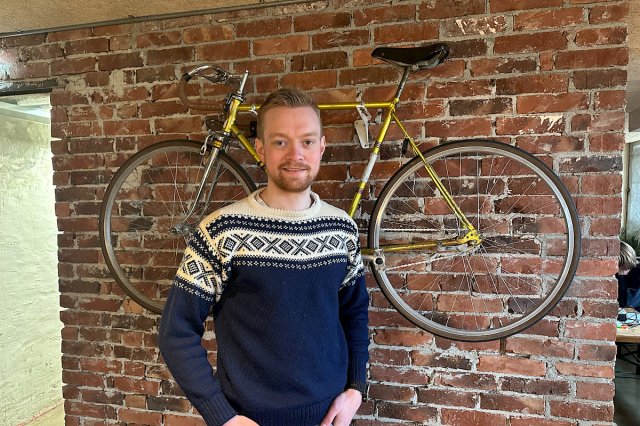 Ung mann foran en murvegg hvor det henger en sykkel