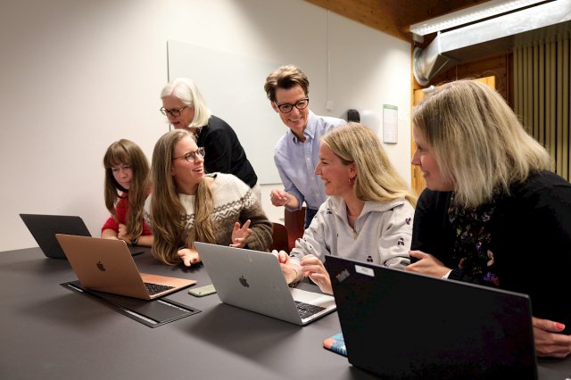 Studenter sitter med laptop og diskuterer sammen med lærere