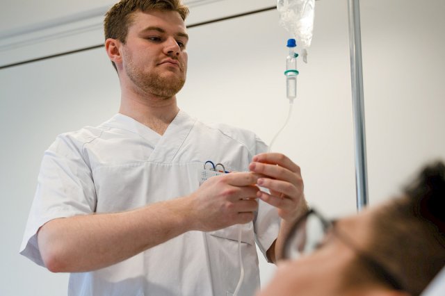 En mannlig sykepleier henger opp en pose med intravenøs væske på stativ