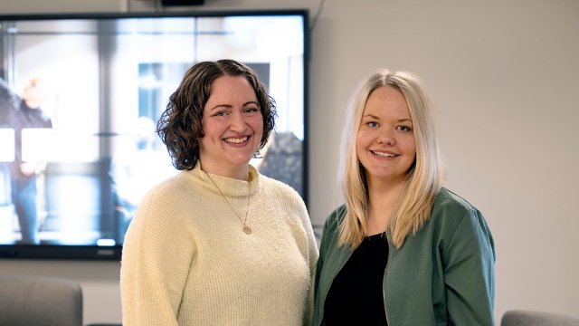 Portrett av to tidligere studenter på studie stående foran whiteboard