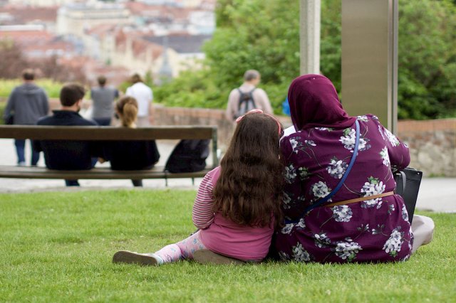 En kvinne med hijab og en ung jente sitter på gresset i en park