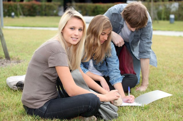 Tre unge studenter sitter på gresset i en park og studerer
