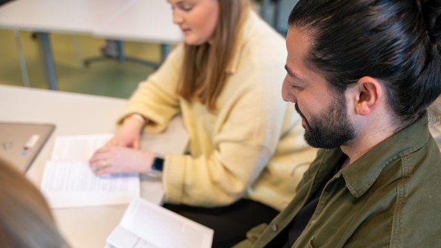 To studenter sitter ved et bord og leser i lærebøker