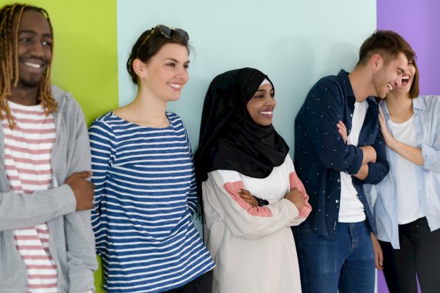 Eng gjeng smilende studenter lener seg mot en vegg