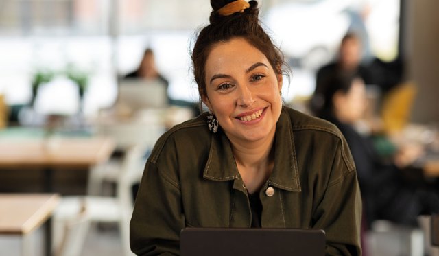 Dame med mørkt hår i hestehale ser i kamera og smiler