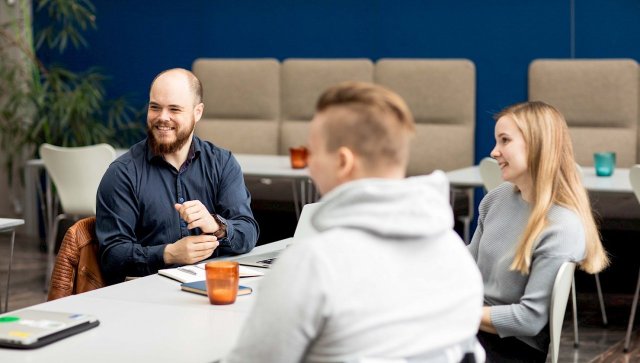 tre studenter som sitter rundt et bord og smiler